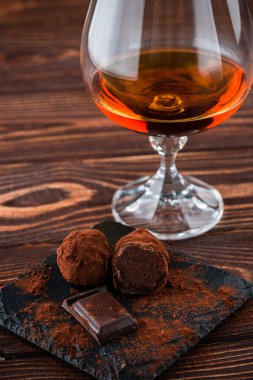Konyaklı çikolatalar, bir bardak brendi ve eski ahşap bir masada çikolatalı mantarlar.