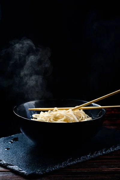 手はスチームと箸麺を保持 黒の背景に蒸し卵麺のボウル アジアの麺ジャンクフードのコンセプト — ストック写真
