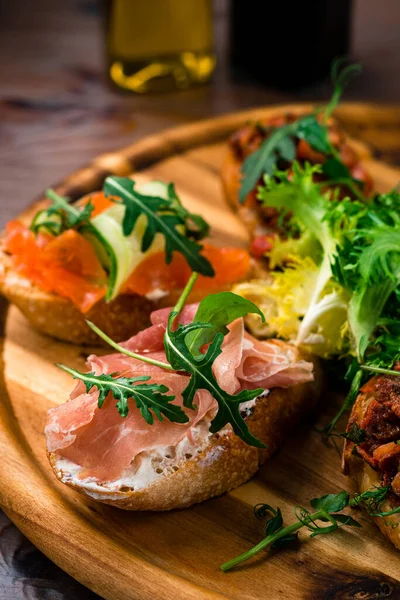Bruschetta con jamón, queso, tomates, hierbas en una tabla de madera. Sabroso desayuno. —  Fotos de Stock