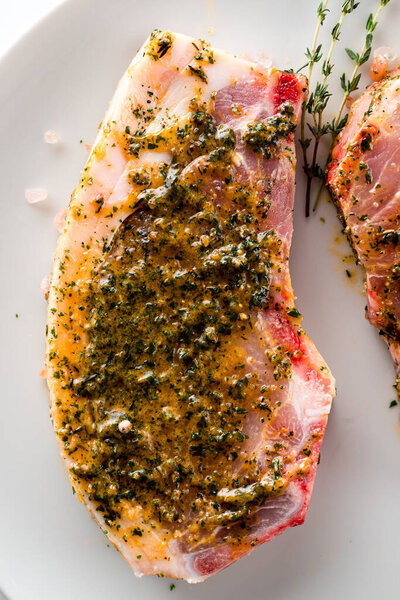 Маринованные сырые свиные отбивные на белой тарелке. Маринованная свинина стейк готов для приготовления пищи, мясо для барбекю, чеснок и травы мариновать. Органический стейк из свинины