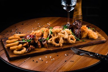 Bira için aperatifler mozarella çubukları, soğan halkaları, patates kızartmaları, tavuk külçeleri ve ahşap bir tahta üzerinde sos.