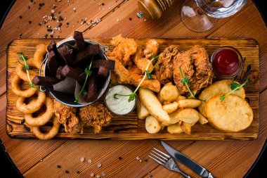 Bira için atıştırmalıklar mozzarella çubukları, soğan halkaları, patates kızartması, tavuk nugget ve ahşap bir tahtanın üzerindeki sos. Bira tabağı, kızarmış parti atıştırmalıkları.