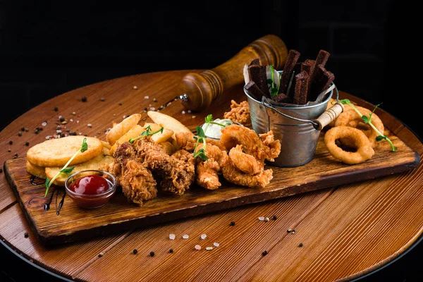 snacks for beer take away food mozzarella sticks, onion rings, french fries, chicken nuggets and sauce on a wooden board. Beer snacks platter, deep fried party snacks