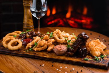 Bira için aperatifler mozarella çubukları, soğan halkaları, patates kızartmaları, tavuk külçeleri ve ahşap bir tahta üzerinde sos.