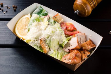 Ahşap arka planda Sezar salatası, yemek teslimatı. Pakette ızgara tavuk filetosu ile klasik sezar salatası.
