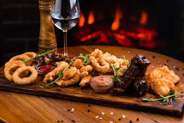 Bira için aperatifler mozarella çubukları, soğan halkaları, patates kızartmaları, tavuk külçeleri ve ahşap bir tahta üzerinde sos.