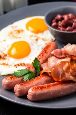 Sosisli kahvaltı, yumurta, pastırma, fasulye, domates ve tost. Tam İngiliz kahvaltısı, karanlık masada.