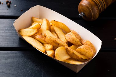 Yemek kutusunda patates dilimleri. Kırsal tarzda kızarmış patates dilimleri kutuya serpiştirilmiş. Fast food restoranında yemek.