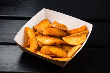 Yemek kutusunda patates dilimleri. Kırsal tarzda kızarmış patates dilimleri kutuya serpiştirilmiş. Fast food restoranında yemek.