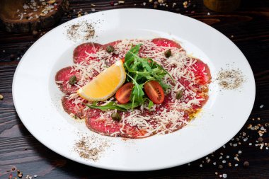 Salata ve limonlu sığır carpaccio, Parmesan peynirli sığır Carpaccio, beyaz tabakta bitki ve vişneli domates.