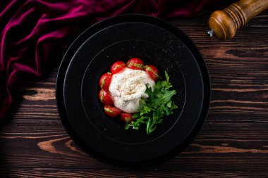 Çeri domatesli burata peyniri geleneksel İtalyan burrata peynirli salata roka ile servis edilir. Burrata İtalyan taze peyniri krema ve bufalo sütü veya inek