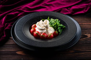 Çeri domatesli burata peyniri geleneksel İtalyan burrata peynirli salata roka ile servis edilir. Burrata İtalyan taze peyniri krema ve bufalo sütü veya inek