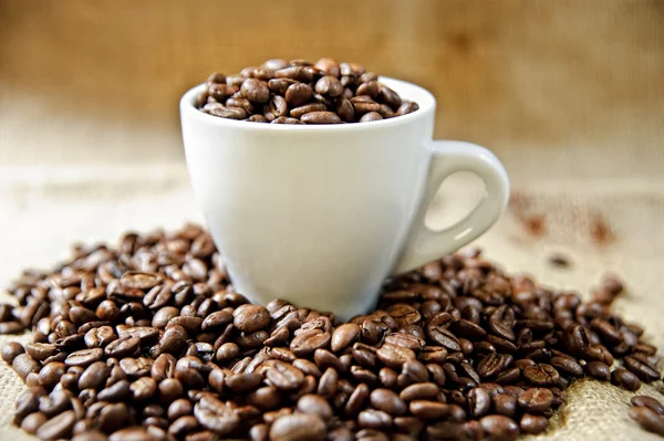 Copo de café branco cheio de grãos de café torrados — Fotografia de Stock