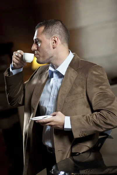 Man dressed on suite drinks cup of coffee inside hotel lobby — Stok fotoğraf