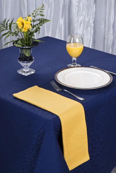 Un paramètre table à manger élégante avec un tissu bleu foncé et une serviette de table jaune. — Photo