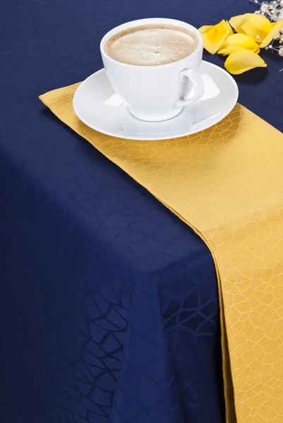 Un ambiente elegante tavolo da pranzo con un panno blu scuro e un tovagliolo giallo con una tazza di caffè — Foto Stock