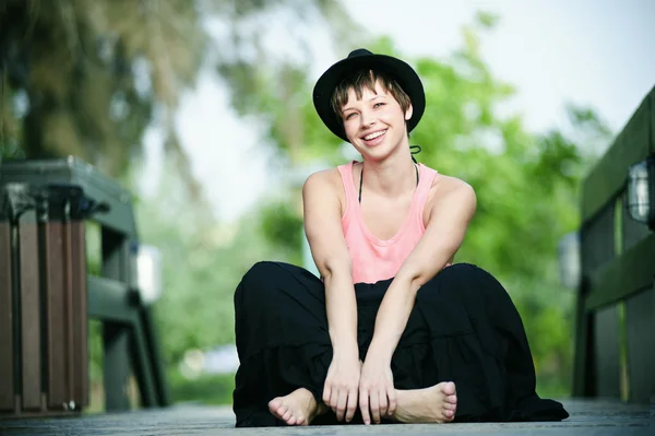 Short hair smiley girl in black hat seating down in the park — Stock Photo, Image