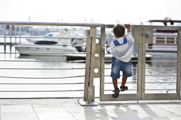 Menino pequeno assistindo curiosamente iates por trás da cerca — Fotografia de Stock