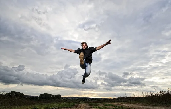 陽男は劇的な夕焼け空の前に高いをジャンプします。 — ストック写真