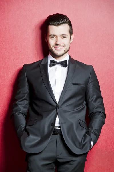 Portrait of yang confident man dressed in tuxedo on red background Royalty Free Stock Images