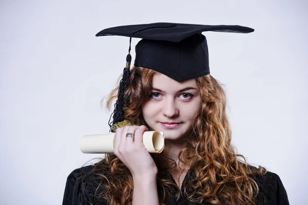 컵과 가운에서 옷을 입고 아름 다운 곱슬 졸업 학생의 스튜디오 초상화 — 스톡 사진