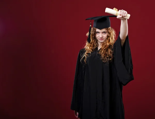Studio portrait of beautiful curly female graduating student dressed in cup and gown — Stock Photo, Image