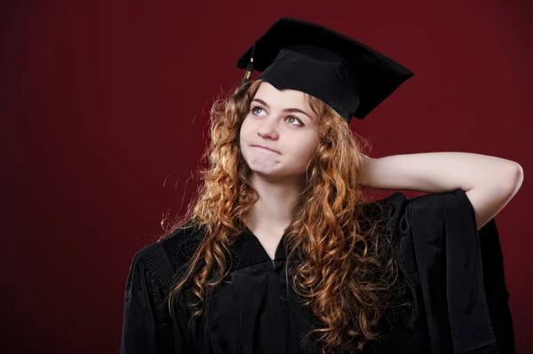 Studio portrait of beautiful curly female graduating student dressed in cup and gown — Stock Photo, Image