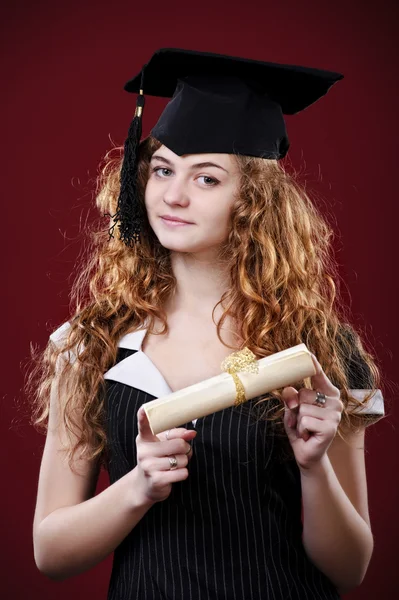 Studio portrait of beautiful curly female graduating student dressed in cup and gown — Stock Photo, Image