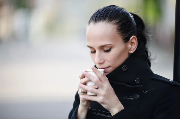 Yang kvinna njuter av kopp kaffe står utomhus — Stockfoto