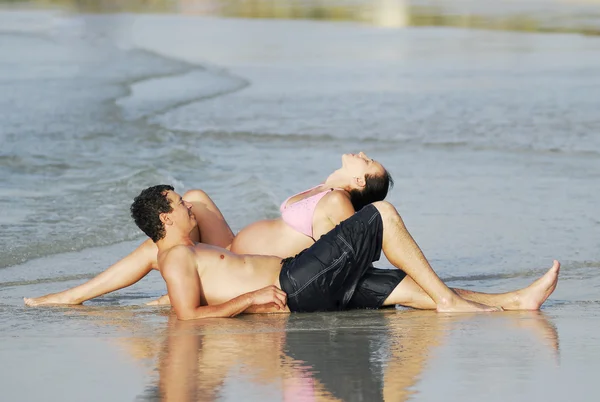 与怀孕的女人放松在海滩上，情侣. — 图库照片