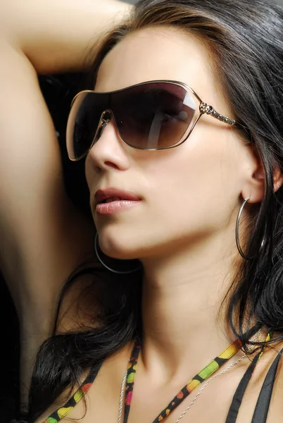 Beautiful brunette woman posing in studio on gray background with sunglasses — Stock Photo, Image