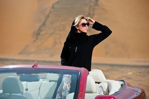 Arabisch gekleidete Frau posiert in rotem Auto in Wüste — Stockfoto
