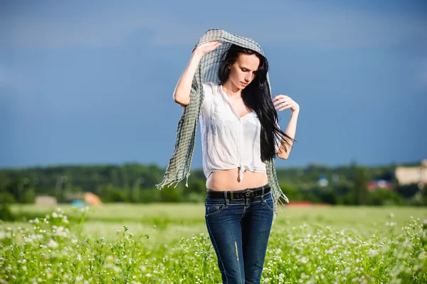 Beautiful brunette poses among green summer field — Stock Photo, Image