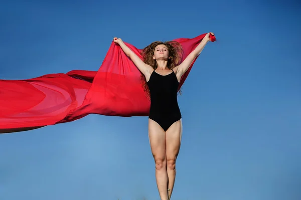 Professional gymnast woman dancer posing in front of sunset sky and red fabric background — Stock Photo, Image