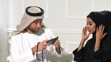 Arap çift evlerinde oturmuş cep telefonu kullanıyor.