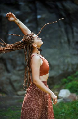 Rastalı güzel bir kız, hippi tarzı giyinmiş, dışarıda poz veriyor..