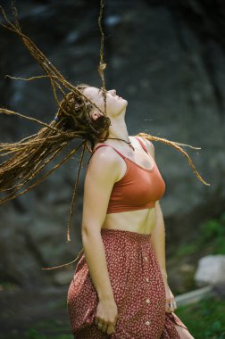 Rastalı güzel bir kız, hippi tarzı giyinmiş, dışarıda poz veriyor..