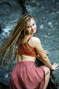 Rastalı güzel bir kız, hippi tarzı giyinmiş, dışarıda poz veriyor..