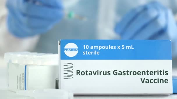 Caixa com vacina contra gastroenterite por rotavírus na mesa contra assistente de laboratório desfocado. Logotipo farmacêutico fictício — Vídeo de Stock