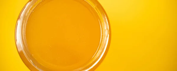 Sklenice organického medu na žlutém pozadí — Stock fotografie