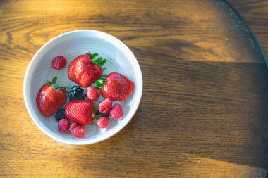 Bir kase suda yüzen taze çilek ve ahududu.