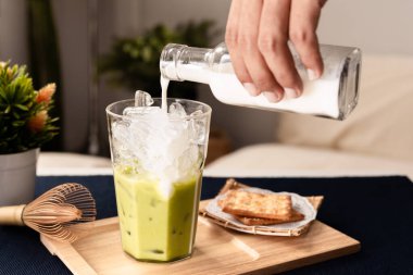Green Tea Latte Iced, The Hands of Brewers Pour Fresh Milk Into a glass of green tea