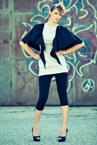 Beautiful fashion model in gray and black garment posing near iron wall — Stock Photo, Image