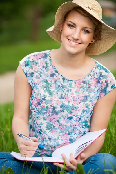 Aantrekkelijke jonge vrouw met een hoed studies op een weide — Stockfoto