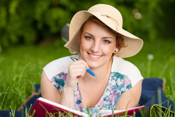 Aantrekkelijke jonge vrouw met een hoed studies op een weide — Stockfoto