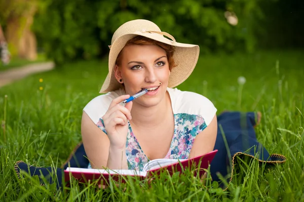 Attractive young woman with a hat studies on a meadow — Stock Photo, Image