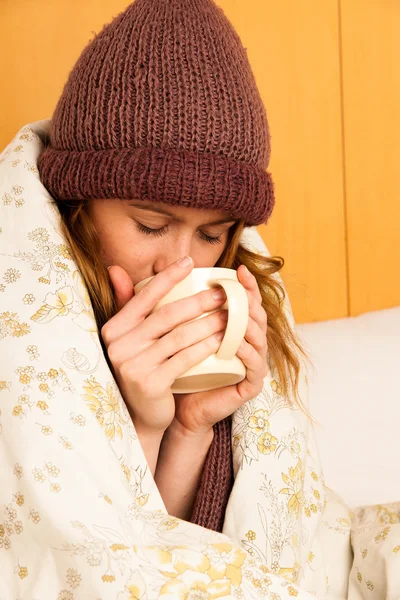 Wanita sakit dengan feaver minum secangkir teh hangat di bawah selimut — Stok Foto