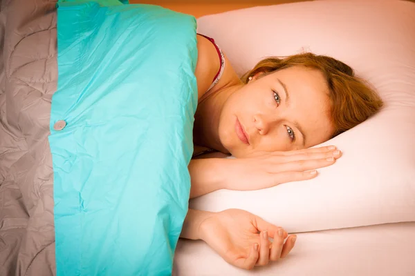 Woman iling on pillow in bed, covered with blanket — Stock Photo, Image