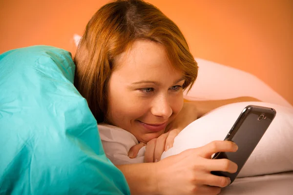Красивая женщина читает смс на телефоне в постели — стоковое фото