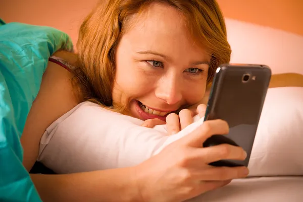 ベッドの中で携帯電話に sms を読んで preety 女性 — ストック写真